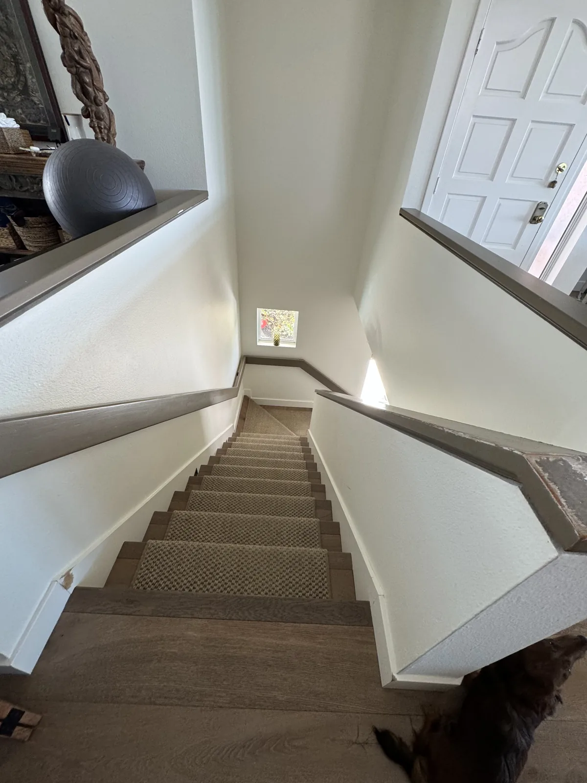 White stairwell walls and trim beside wood steps and a dark handrail