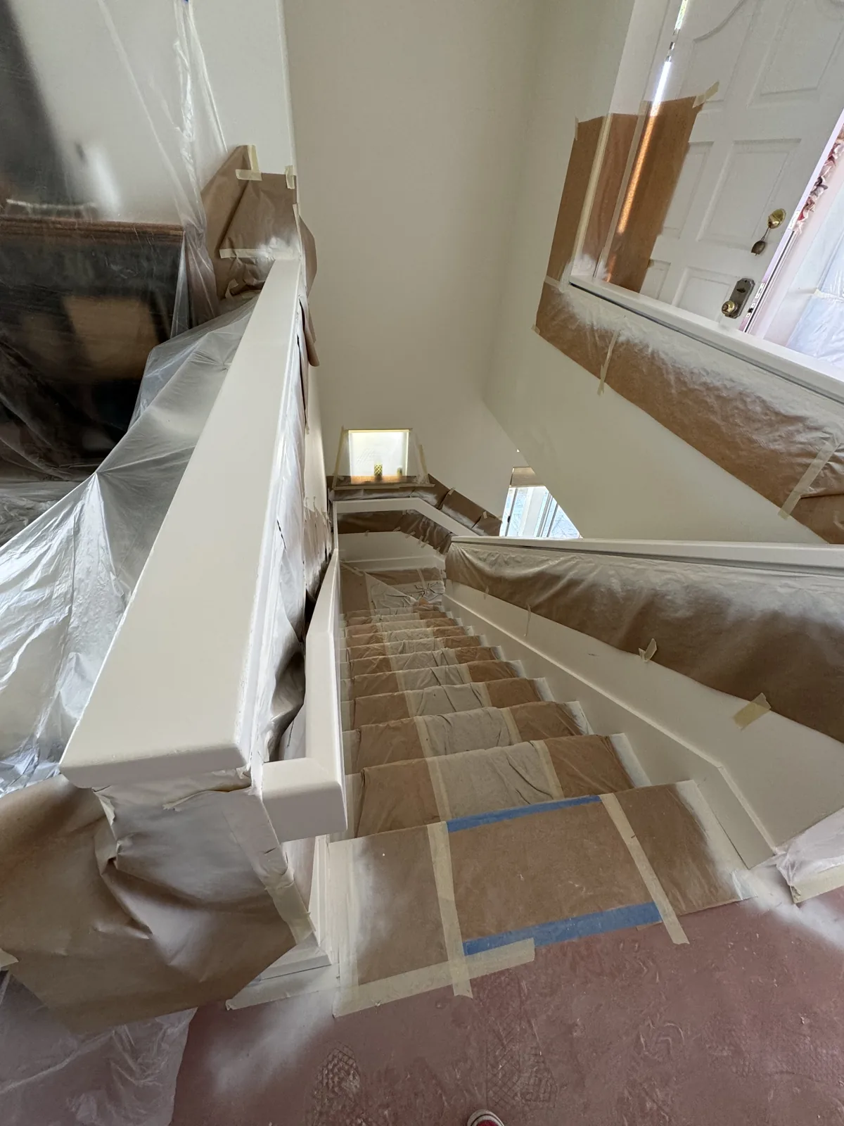 Wood staircase, rails and adjacent interior surfaces covered with plastic and masking tape