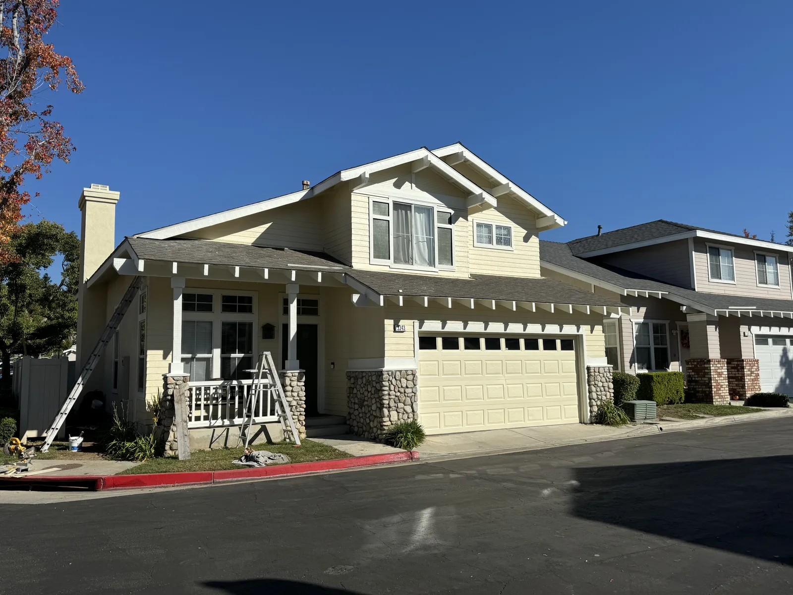 Craftsman-style two-story house with white trim, stone porch columns and ladders against the porch