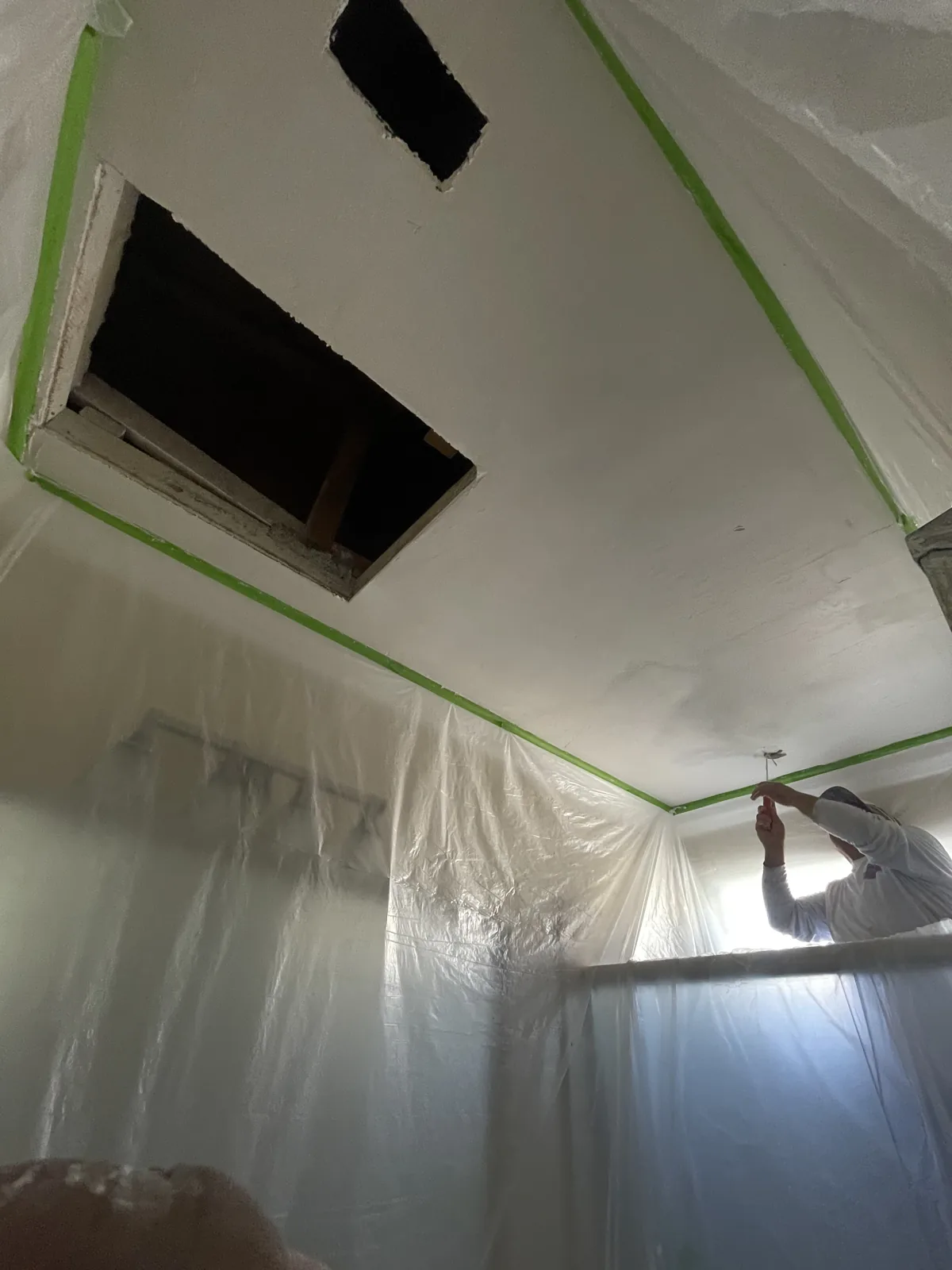 Open ceiling repair areas with green tape and plastic protection over surrounding walls